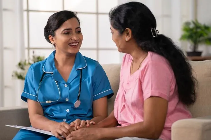 A healthcare professional speaking with a woman seated beside her.